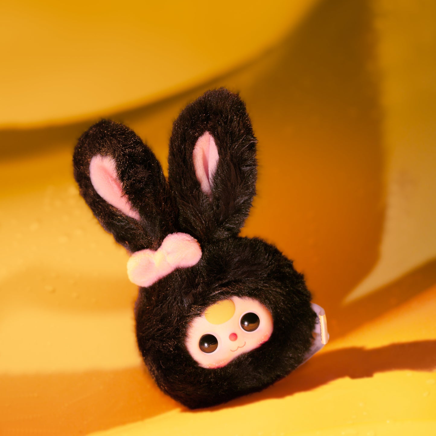 Plush toy with black fur, pink bow, and white face on a yellow background